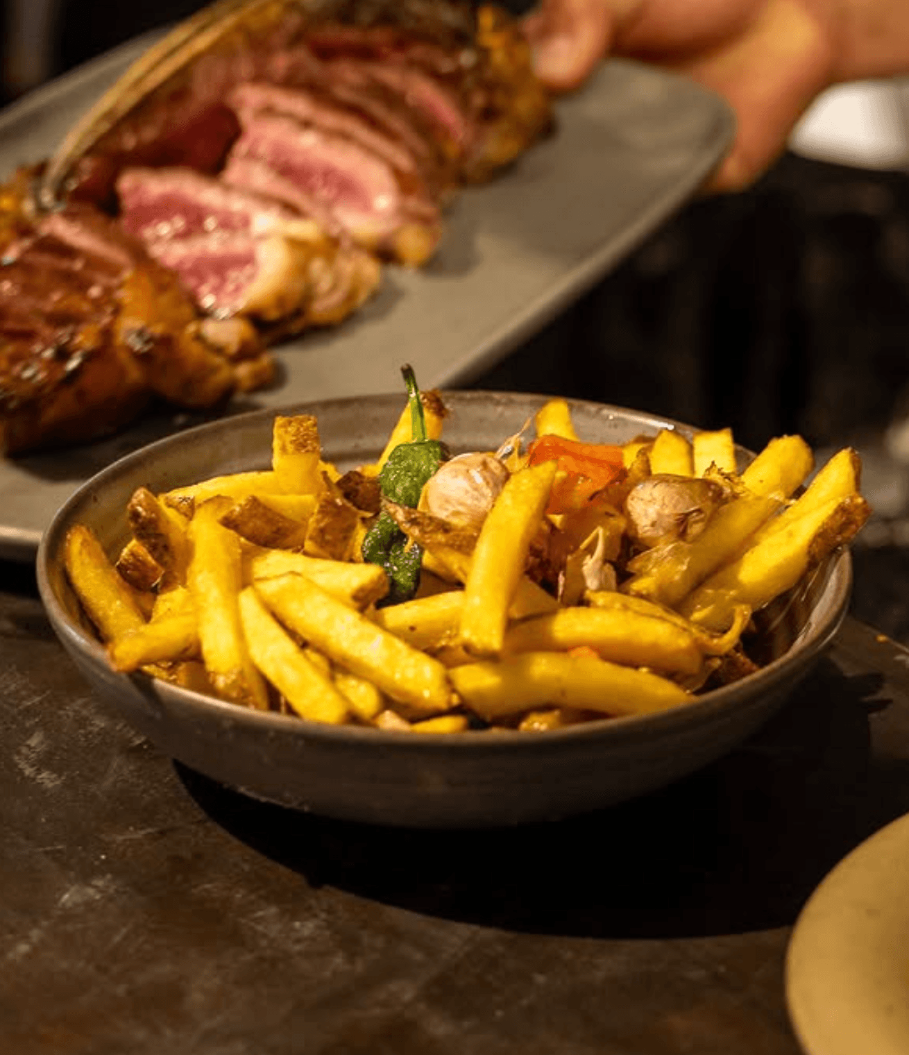 Patatas fritas con ajos y pimientos, con el chuletón al fondo
